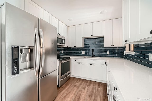 kitchen featuring white cabinetry, sink, decorative backsplash, light hardwood / wood-style floors, and stainless steel appliances