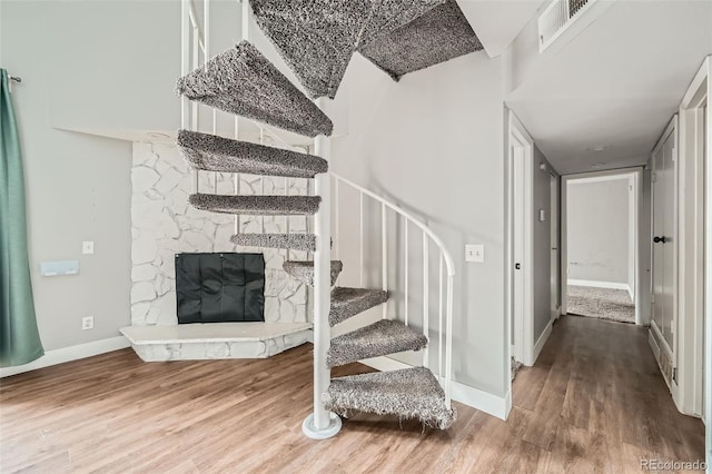 stairway featuring hardwood / wood-style flooring and a stone fireplace