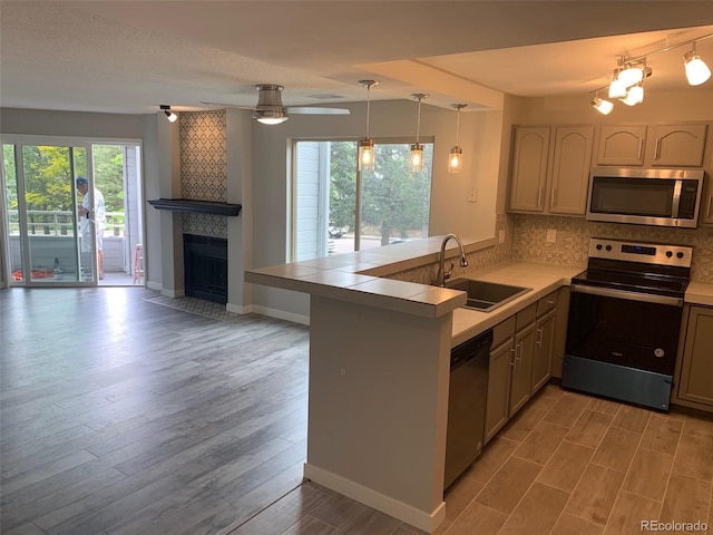 kitchen featuring stainless steel appliances, light wood-style floors, a sink, a tile fireplace, and a peninsula