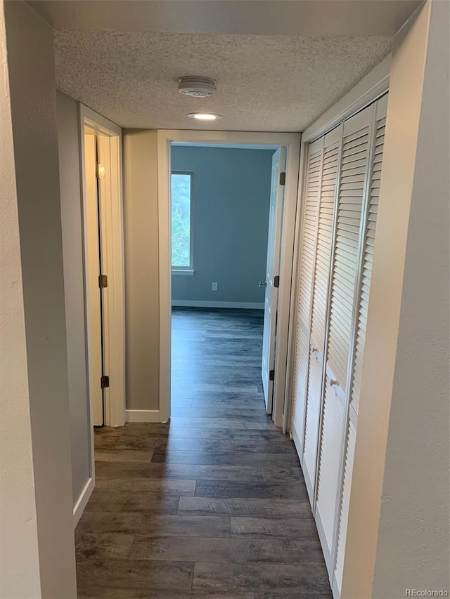 hall with a textured ceiling, dark wood-style flooring, and baseboards