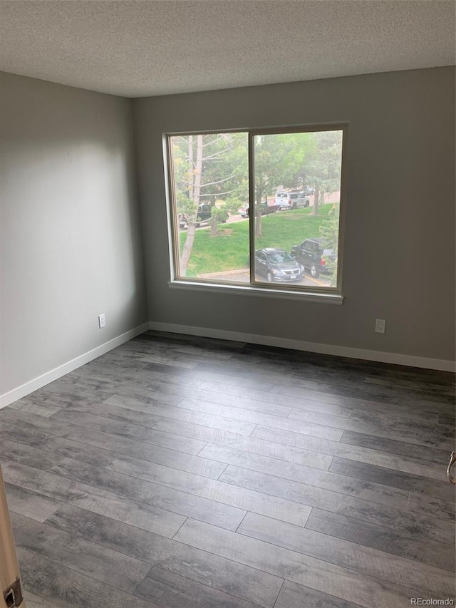 spare room with a textured ceiling, baseboards, and wood finished floors