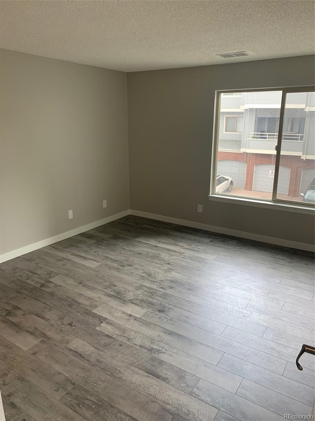 spare room featuring visible vents, a textured ceiling, baseboards, and wood finished floors