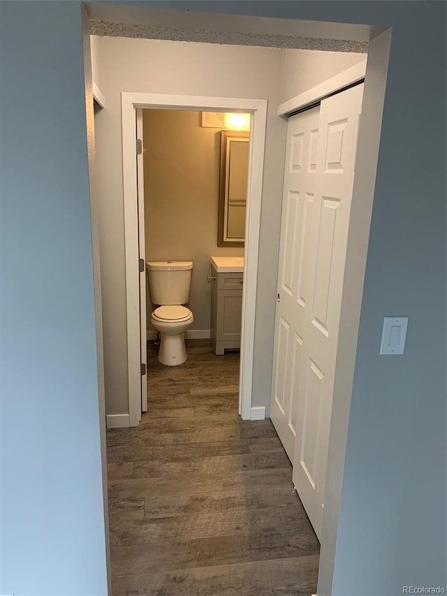 half bathroom with vanity, wood finished floors, toilet, and baseboards