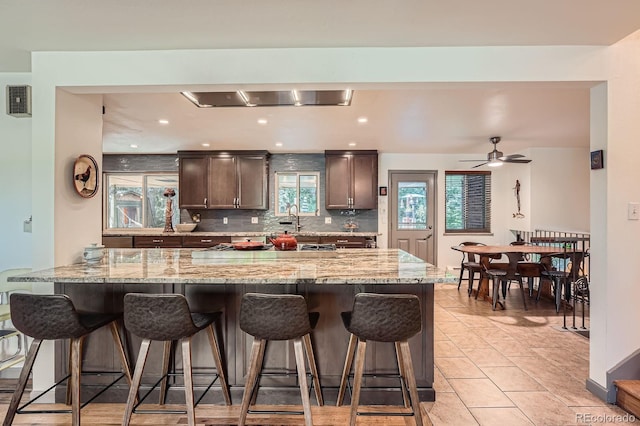7875 W 21st Ave, Lakewood, CO 80214 - kitchen with a breakfast bar area, tasteful backsplash, dark brown cabinetry, light stone countertops, and a ceiling fan