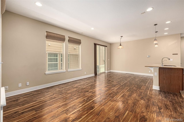 unfurnished living room with recessed lighting, baseboards, dark wood-style flooring, and a sink