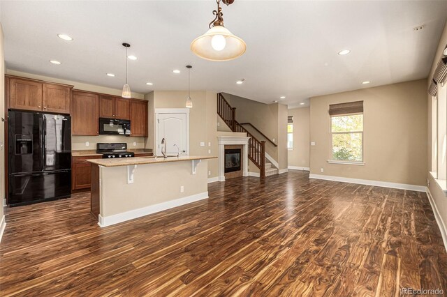 kitchen with dark wood-type flooring, black appliances, a kitchen breakfast bar, a center island with sink, and decorative light fixtures