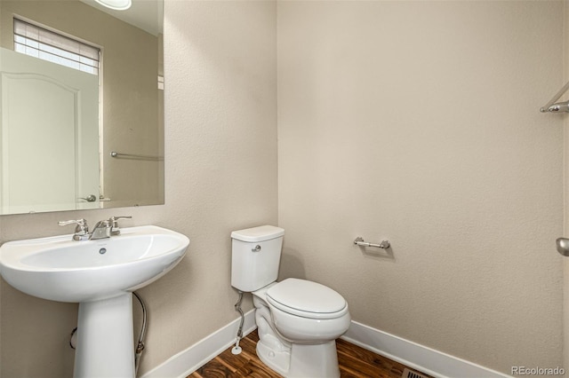 half bath featuring toilet, wood finished floors, baseboards, and a sink