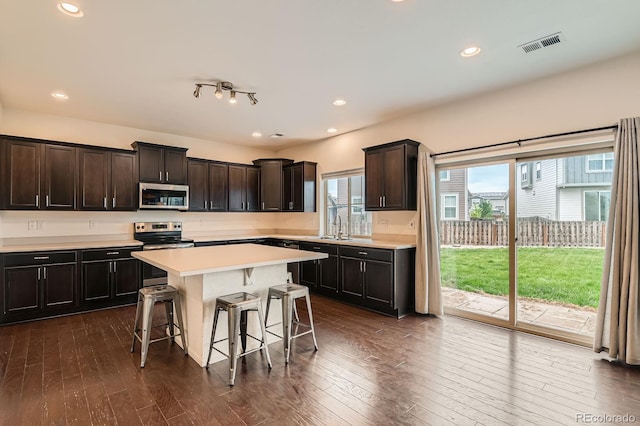 12981 E 108th Way, Commerce City, CO 80022 - kitchen featuring appliances with stainless steel finishes, dark wood finished floors, a kitchen breakfast bar, light countertops, and a center island