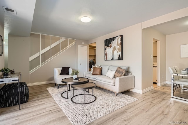 living room featuring light wood-style flooring, baseboards, and stairs