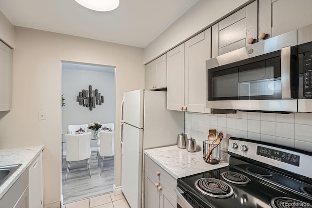 kitchen featuring stainless steel appliances, decorative backsplash, light tile patterned flooring, light stone counters, and a sink