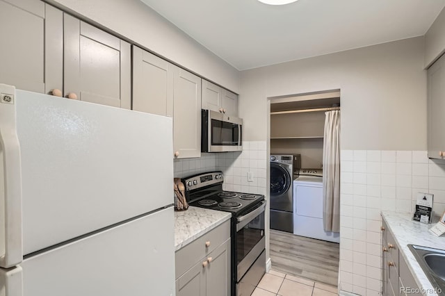 kitchen featuring appliances with stainless steel finishes, separate washer and dryer, light tile patterned floors, gray cabinets, and tile walls