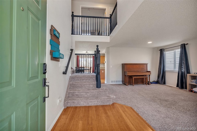 carpeted entryway featuring visible vents, baseboards, a textured ceiling, and stairs