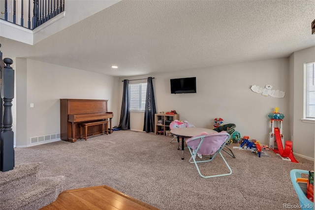 recreation room featuring a textured ceiling, visible vents, carpet flooring, and baseboards