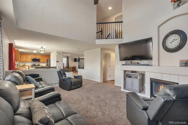 living room featuring a tiled fireplace, baseboards, recessed lighting, a high ceiling, and carpet floors