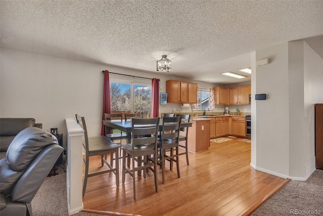 dining space with baseboards, a textured ceiling, and light wood-style flooring