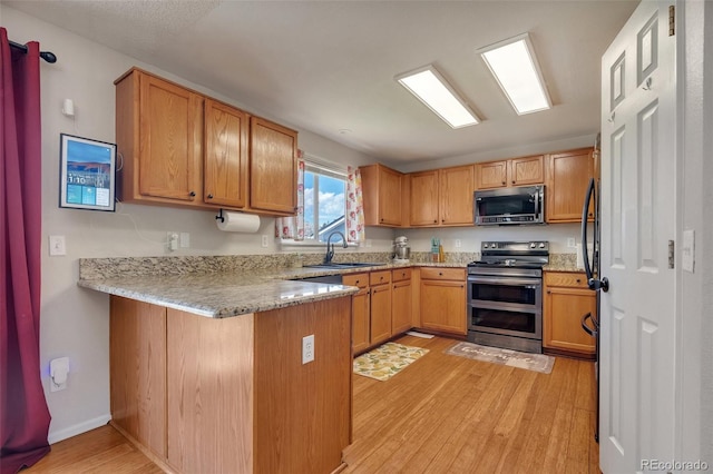 kitchen with stainless steel appliances, a peninsula, a sink, light wood-style floors, and light stone counters