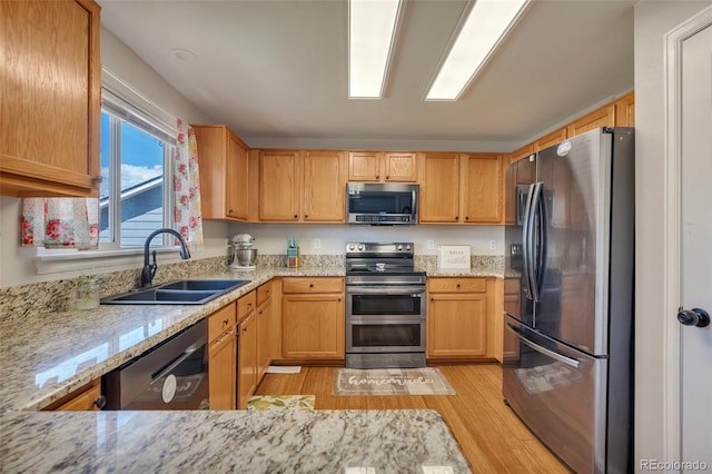 kitchen with appliances with stainless steel finishes, light stone countertops, a sink, and light wood-style flooring