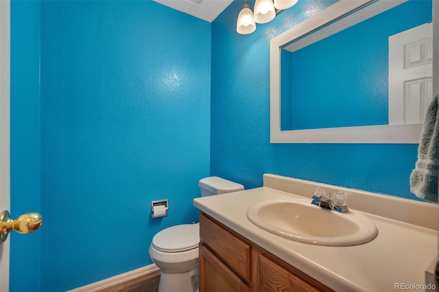 bathroom with toilet, baseboards, wood finished floors, a textured wall, and vanity