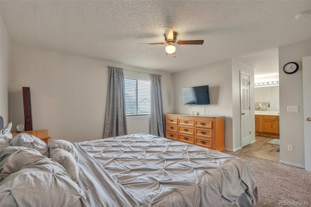 bedroom featuring ensuite bath, light carpet, a ceiling fan, and a textured ceiling