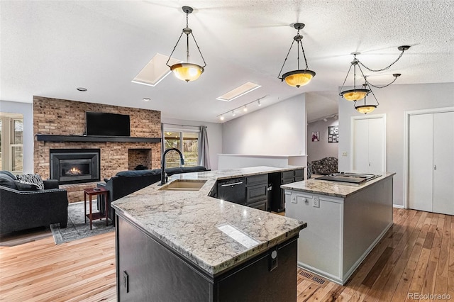 kitchen with an island with sink, a sink, light wood-style flooring, and a fireplace