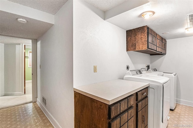 laundry room featuring cabinet space, a textured ceiling, baseboards, light floors, and washing machine and dryer