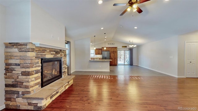 unfurnished living room featuring ceiling fan with notable chandelier, dark hardwood / wood-style flooring, a stone fireplace, and vaulted ceiling