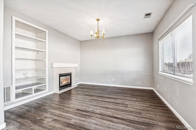 unfurnished living room with an inviting chandelier, dark wood-type flooring, built in features, and a tile fireplace