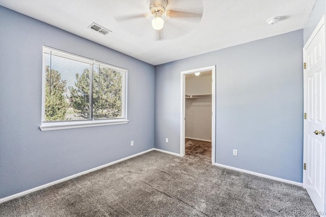 unfurnished bedroom featuring carpet flooring, a spacious closet, ceiling fan, and a closet