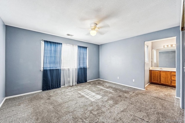 unfurnished bedroom featuring ceiling fan, carpet floors, ensuite bath, and a textured ceiling