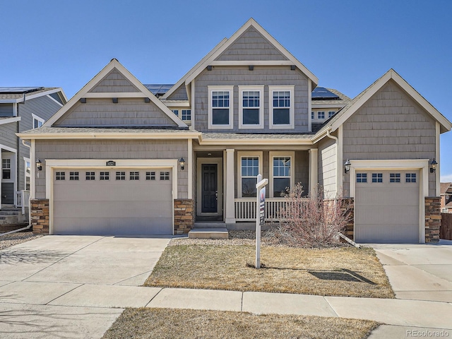 craftsman-style house with a porch, a garage, solar panels, driveway, and stone siding