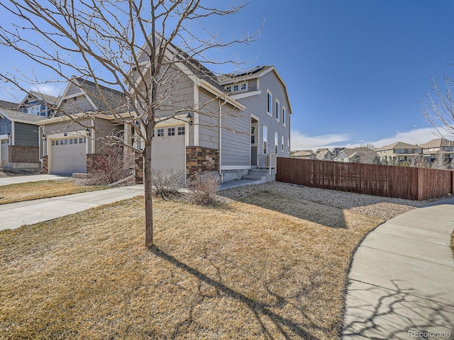 view of property exterior with fence, a garage, a residential view, stone siding, and driveway