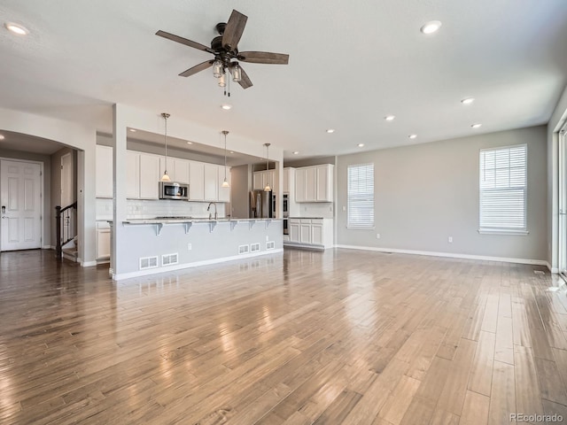 unfurnished living room featuring plenty of natural light, baseboards, arched walkways, and wood finished floors