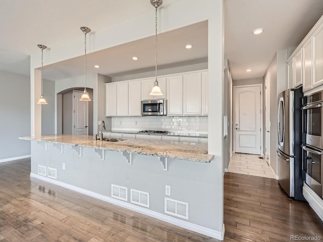 kitchen with dark wood-style floors, stainless steel appliances, visible vents, a sink, and a kitchen bar