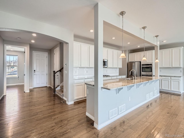 kitchen featuring white cabinets, arched walkways, stainless steel appliances, and wood finished floors