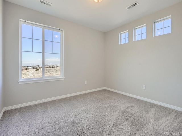 carpeted spare room featuring a healthy amount of sunlight, baseboards, and visible vents