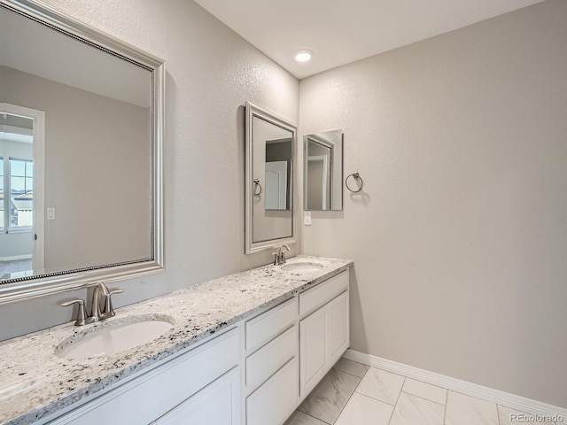 bathroom with marble finish floor, double vanity, a sink, and baseboards