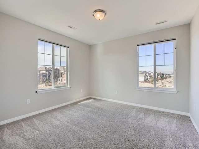 unfurnished room with carpet floors, a wealth of natural light, visible vents, and baseboards