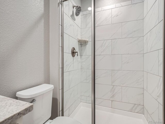 full bathroom featuring toilet, a shower stall, and a textured wall