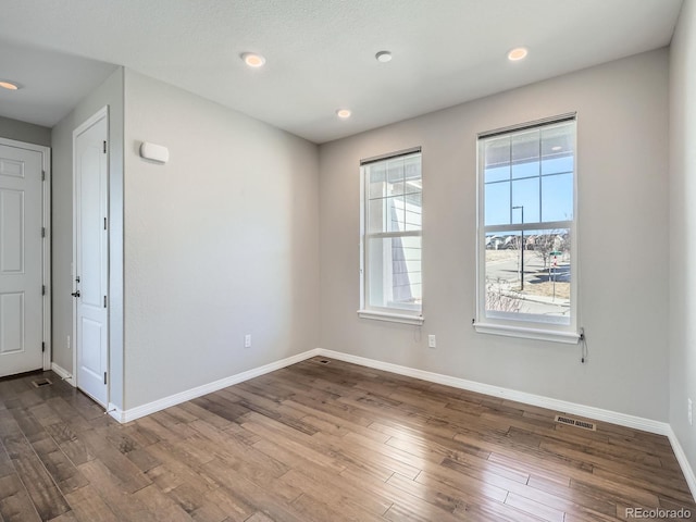 unfurnished room with dark wood-style floors, visible vents, and baseboards