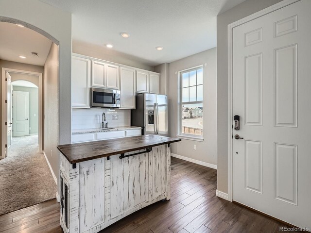 kitchen with arched walkways, a sink, wood counters, appliances with stainless steel finishes, and tasteful backsplash