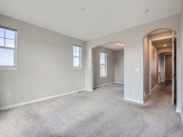 empty room with light carpet, visible vents, baseboards, and arched walkways