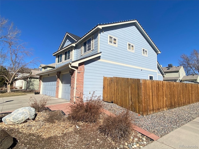 view of property exterior with brick siding, fence, driveway, and an attached garage