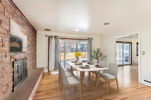 dining space featuring baseboard heating, a large fireplace, plenty of natural light, and light wood-type flooring