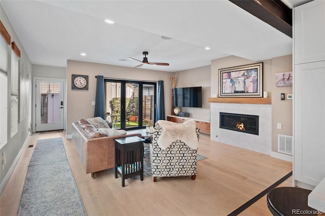 living area with a glass covered fireplace, recessed lighting, visible vents, ceiling fan, and light wood finished floors