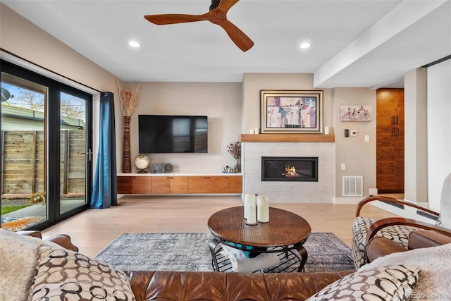 living room with recessed lighting, a tiled fireplace, light wood-style flooring, a ceiling fan, and visible vents