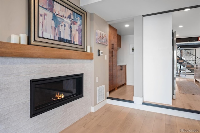 unfurnished living room featuring visible vents, baseboards, wood finished floors, stairs, and a glass covered fireplace