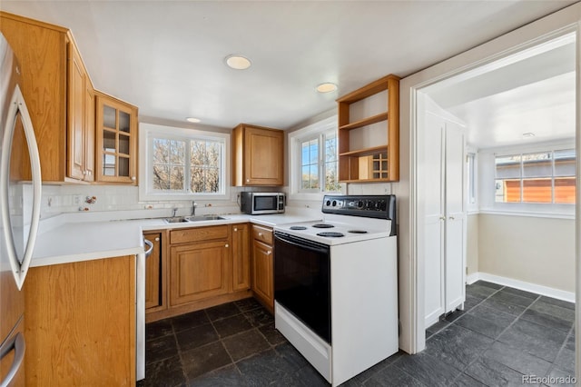 kitchen with a sink, backsplash, appliances with stainless steel finishes, light countertops, and glass insert cabinets