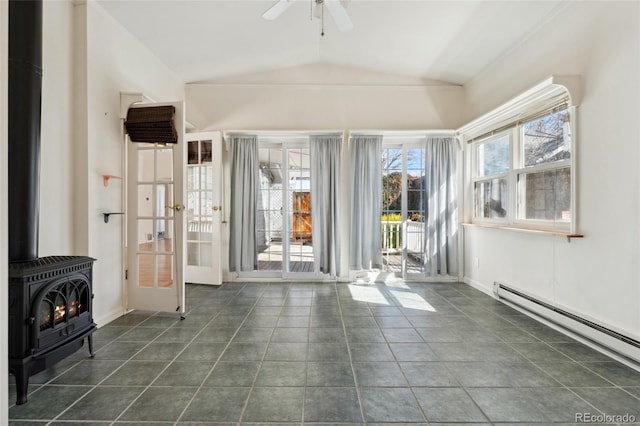 unfurnished room with dark tile patterned floors, a ceiling fan, lofted ceiling, baseboard heating, and a wood stove