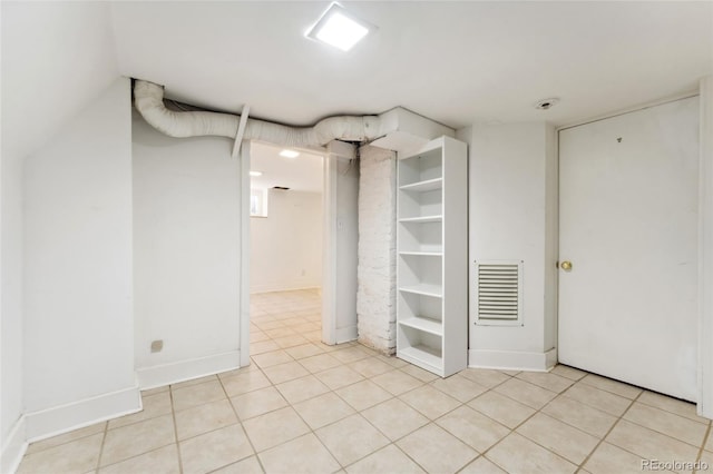 finished below grade area with light tile patterned floors, visible vents, built in shelves, and baseboards