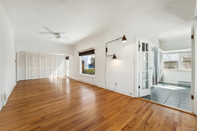 unfurnished living room featuring a baseboard heating unit, plenty of natural light, a ceiling fan, and hardwood / wood-style flooring